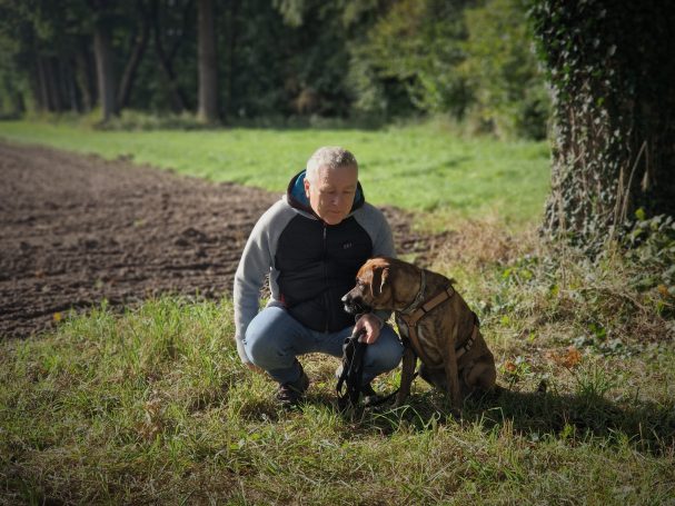 Ein Mann kniet neben einem braunen Hund auf einer Wiese.